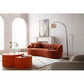 Modern curved boucle fabric 3 seat sofa in a living room with orange accent tables and floor lamp.