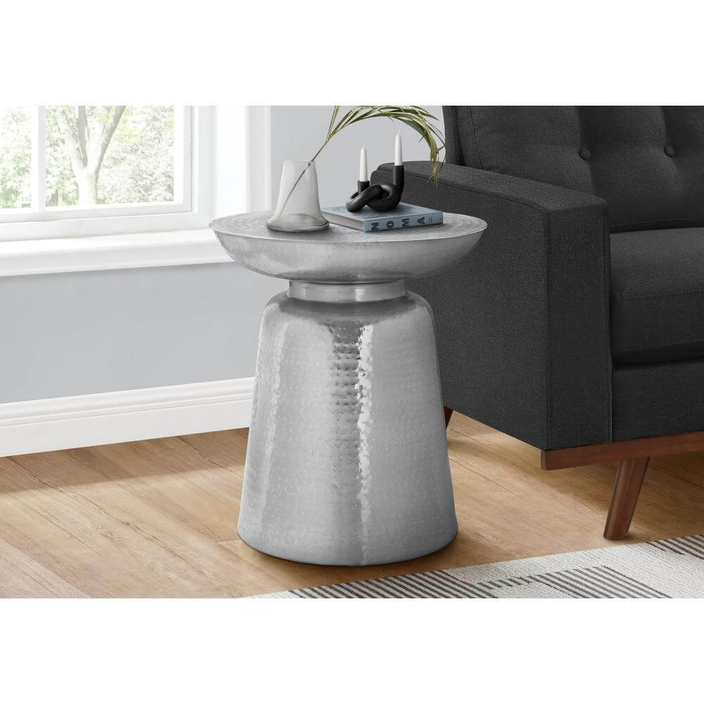 Hammered metal round drum accent end table in white with bell-shaped base next to a gray sofa in a modern living room